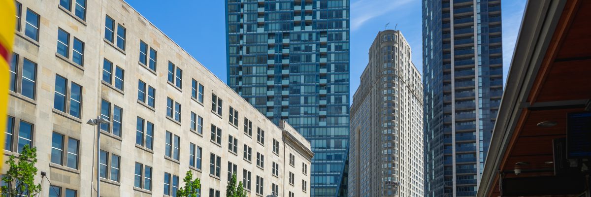 Two tall buildings in the background with a flat iron building in the middle. On the left is a midrise building, and on the right is a green and white GO bus.