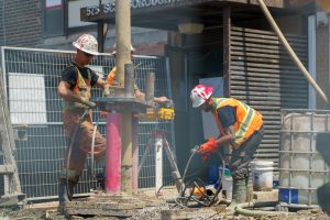 Two construction workers assist in borehole excavation