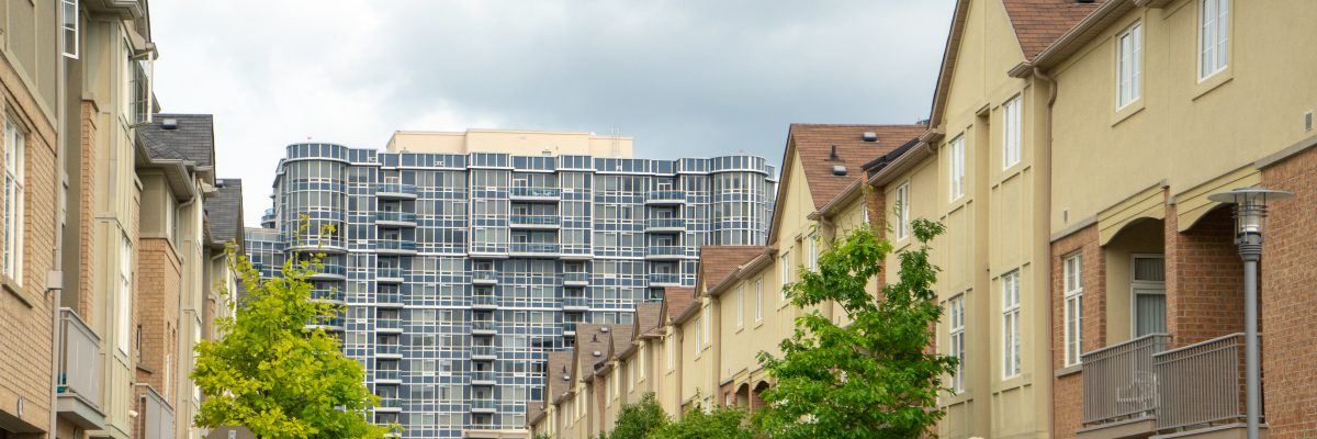 A row of beige townhouses on either side of a street, with a taller condo building in the background