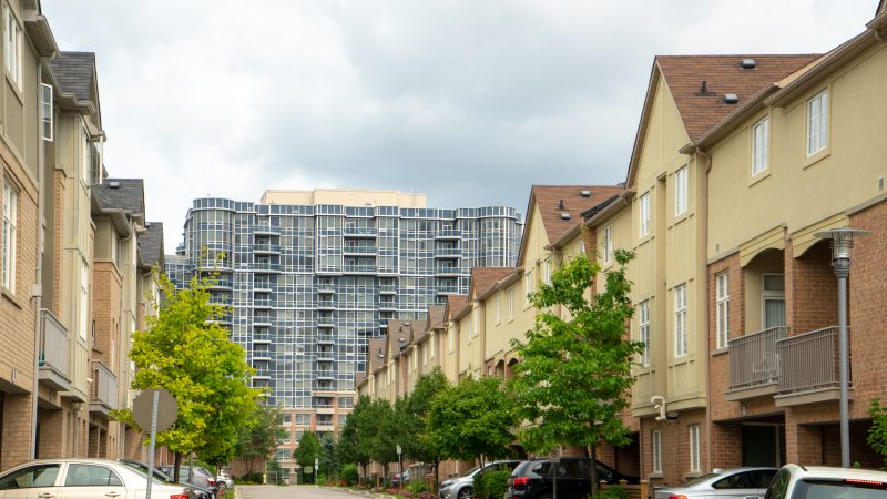 A row of beige townhouses on either side of a street, with a taller condo building in the background
